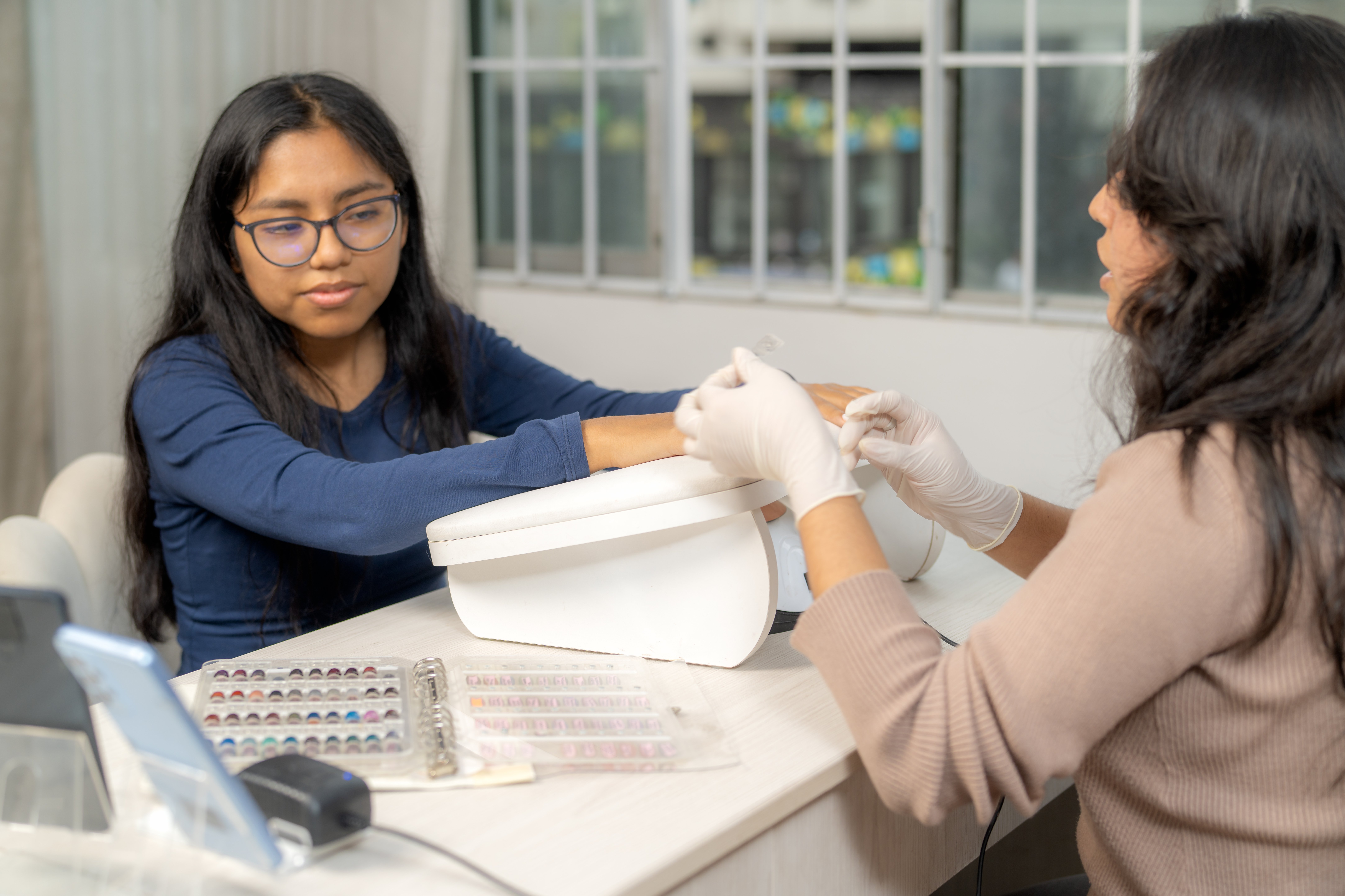 Professional nail technician wearing gloves applying a new manicure to a female client's nails in a modern beauty salon
